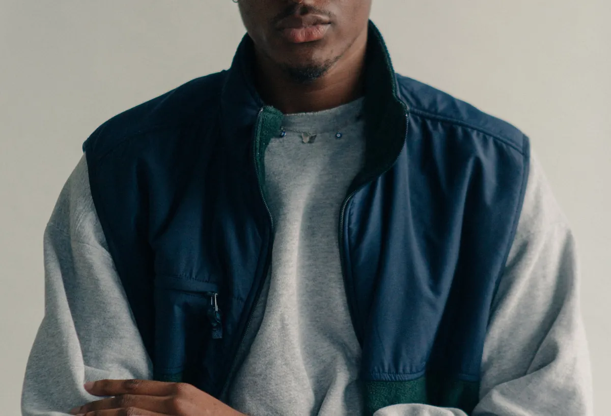 Man wearing a navy zip-up vest with green fleece trim over a heather grey sweatshirt