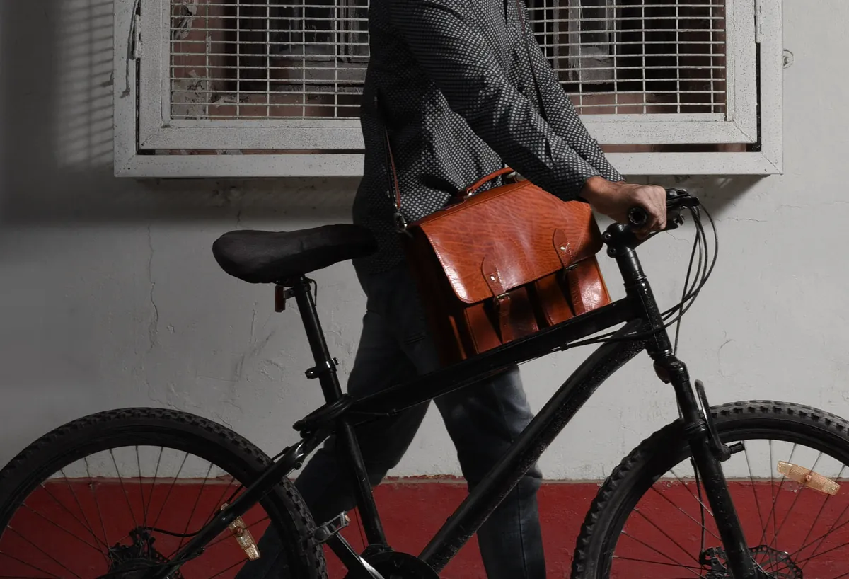 Man with a bicycle wearing a tan leather messenger bag across his body