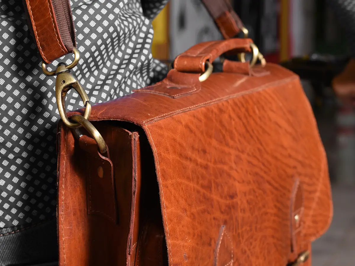 Close-up of a tan leather messenger bag with flap, buckles and brass clasp