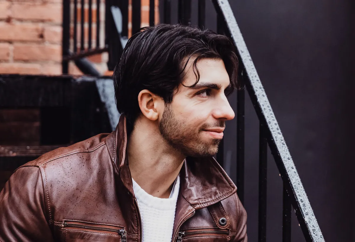 Man in a brown leather jacket and white sweater, sitting on a brick stairway