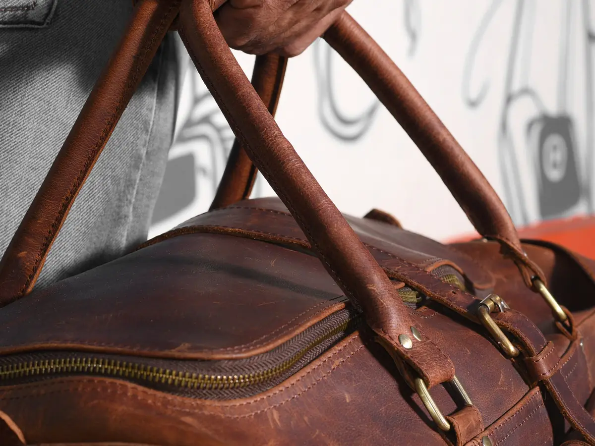 Gros plan sur les anses en cuir brun d'un sac, fixées par des anneaux et des boucles en laiton